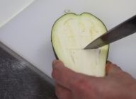 米茄子を縦半分に切り、断面に食べやすいように外側にぐるりと一周、内側に縦1本、6～8等分になるように2、3本横に切り込みを皮の手前まで刃を入れる。