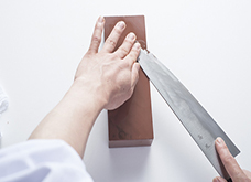 支える手の指で刃先の腹を押さえ、包丁の刃先の面が研ぎ石に当たるように包丁を持つ手を少し持ち上げ、ほんのわずかの角度をつける。